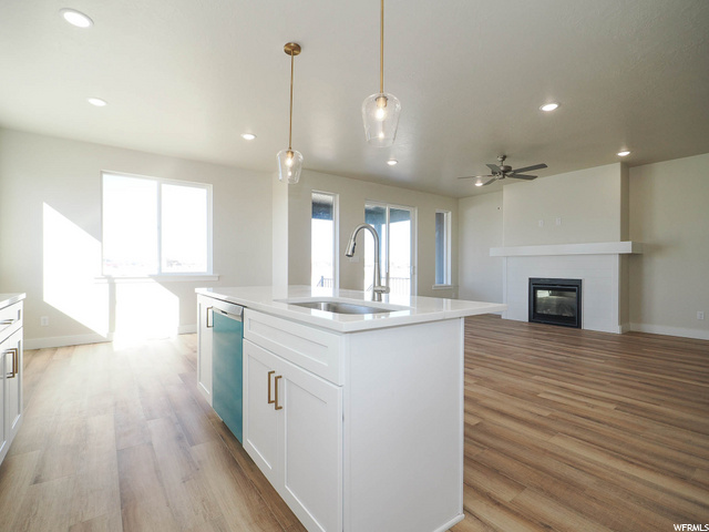 kitchen featuring a fireplace, natural light, a ceiling fan, dishwasher, light parquet floors, pendant lighting, light countertops, and an island with sink