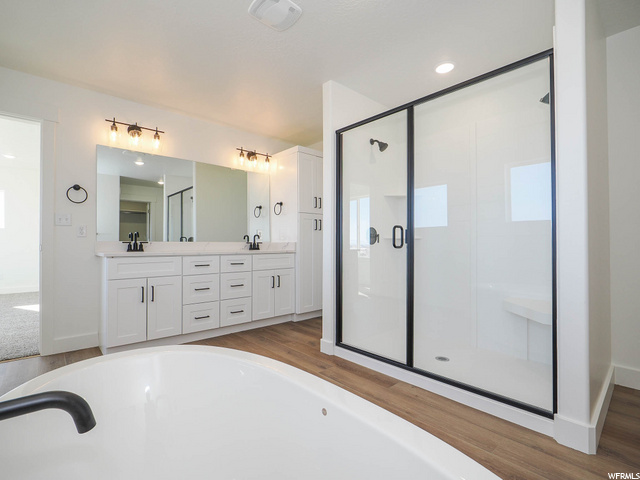 bathroom featuring wood-type flooring, separate shower and tub, dual large bowl vanity, and mirror
