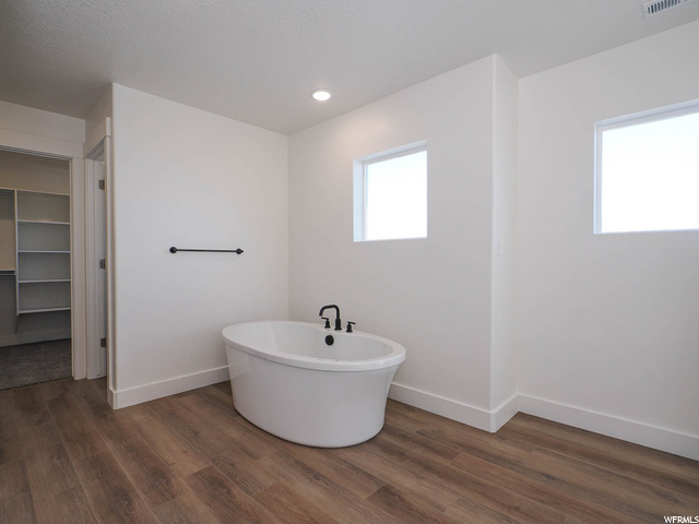 bathroom with natural light, hardwood flooring, and a bath