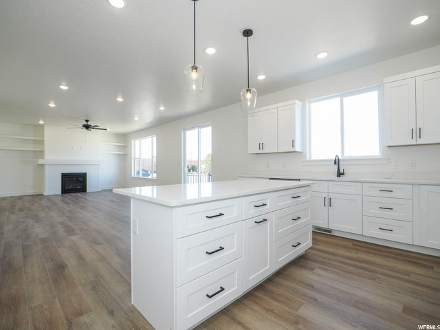 kitchen with natural light, hardwood flooring, a ceiling fan, a fireplace, white cabinetry, light stone countertops, and pendant lighting