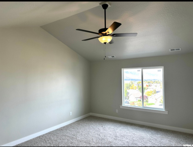 spare room featuring carpet, natural light, a ceiling fan, and lofted ceiling