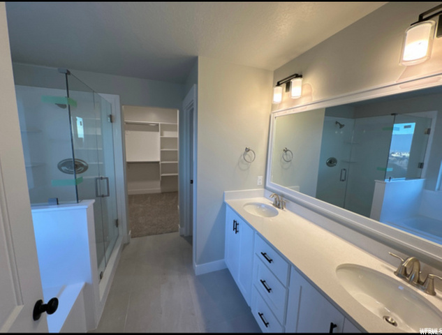 bathroom with wood-type flooring, double large vanities, mirror, shower with glass door, and his and her basins
