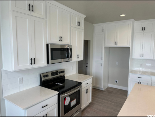 kitchen featuring electric range oven, microwave, light countertops, white cabinetry, and dark hardwood floors