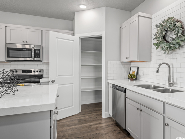 kitchen featuring stainless steel dishwasher, range oven, microwave, white cabinets, light countertops, and dark hardwood flooring