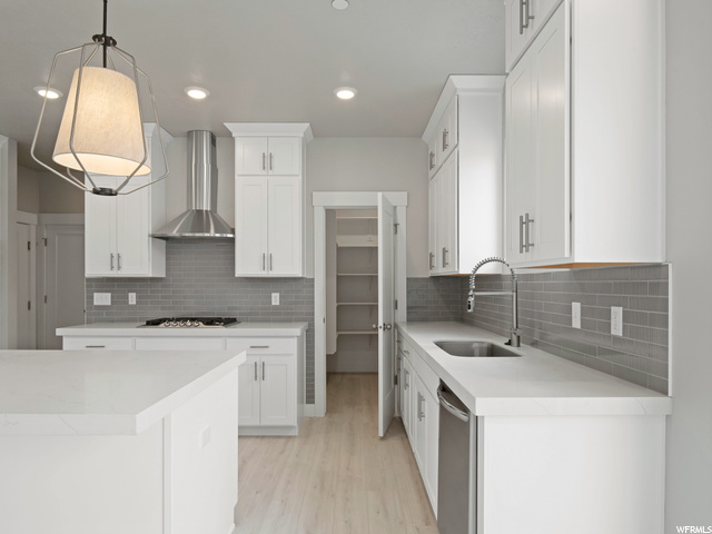 kitchen featuring hardwood floors, fume extractor, dishwasher, gas cooktop, pendant lighting, white cabinetry, and light countertops