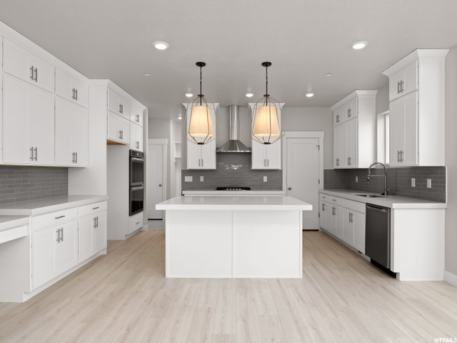 kitchen featuring a kitchen island, stainless steel appliances including a double oven, extractor fan, pendant lighting, light hardwood floors, light countertops, and white cabinets
