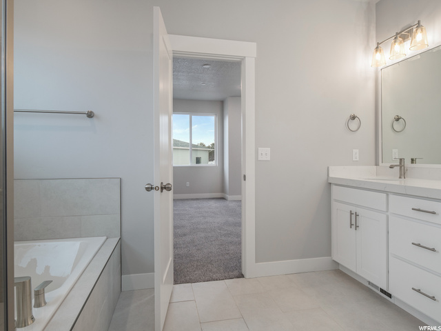bathroom featuring tile flooring, vanity, mirror, and a tub