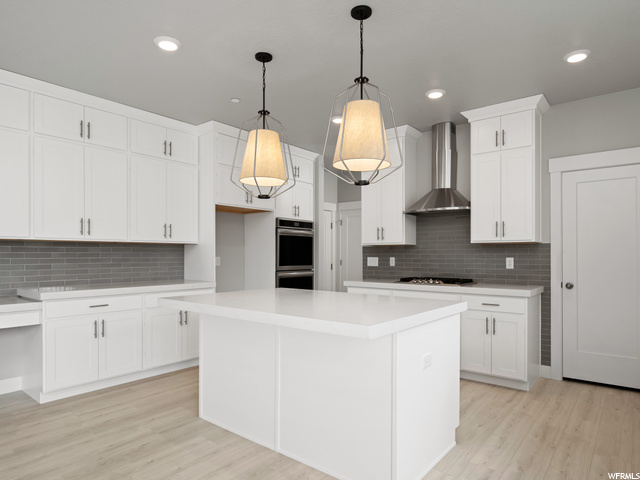 kitchen featuring a center island, gas stovetop, double oven, fume extractor, pendant lighting, light hardwood floors, light countertops, and white cabinetry