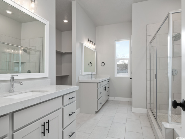 bathroom featuring natural light, tile floors, mirror, shower booth, and dual vanity