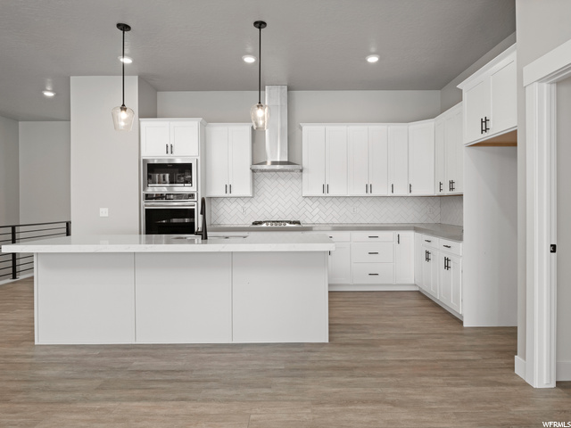 kitchen with ventilation hood, oven, microwave, light parquet floors, pendant lighting, light countertops, and white cabinetry