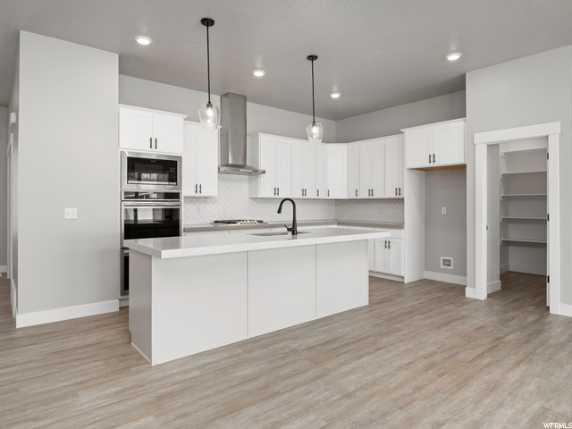 kitchen with ventilation hood, oven, pendant lighting, white cabinets, light parquet floors, light countertops, and a kitchen island with sink