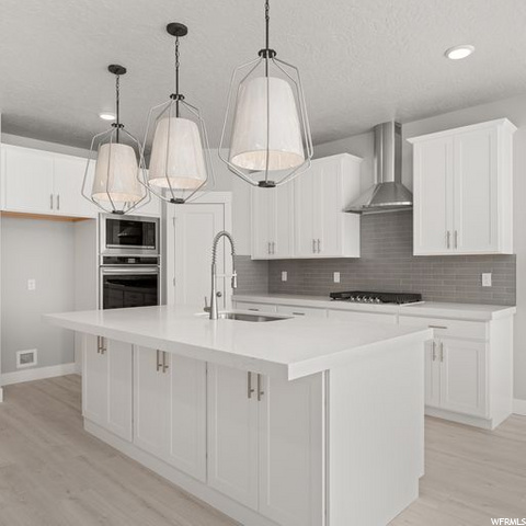 kitchen featuring oven, gas stovetop, fume extractor, microwave, pendant lighting, white cabinets, a center island with sink, light parquet floors, and light countertops