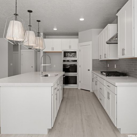 kitchen with stainless steel double oven, gas stovetop, light parquet floors, pendant lighting, white cabinetry, and light countertops