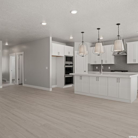 kitchen with stainless steel double oven, microwave, fume extractor, light parquet floors, pendant lighting, white cabinetry, and light countertops