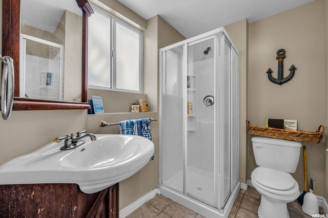 full bathroom with tile floors, washbasin, toilet, shower with shower door, and mirror