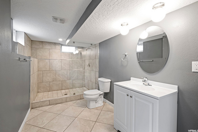 bathroom with tile floors, toilet, vanity, mirror, and a shower