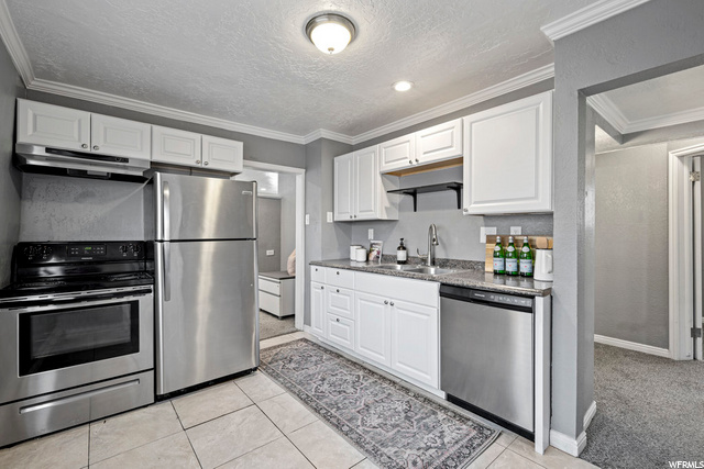 kitchen featuring refrigerator, electric range oven, dishwasher, extractor fan, white cabinetry, and light tile flooring