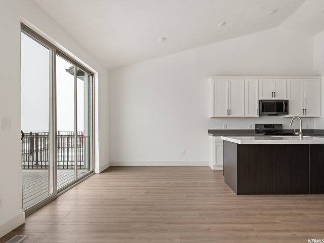 kitchen with natural light, lofted ceiling, range oven, microwave, white cabinets, light countertops, and light hardwood floors