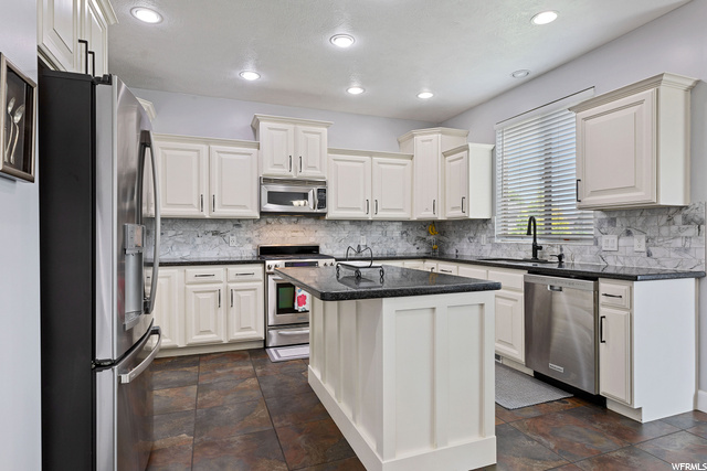 Kitchen featuring natural light, microwave, range oven, stainless steel dishwasher, refrigerator, white cabinets, dark granite-like countertops, and dark tile floors