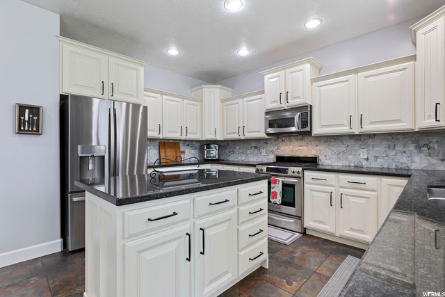 Kitchen featuring microwave, range oven, white cabinets, dark granite-like countertops, and dark tile floors