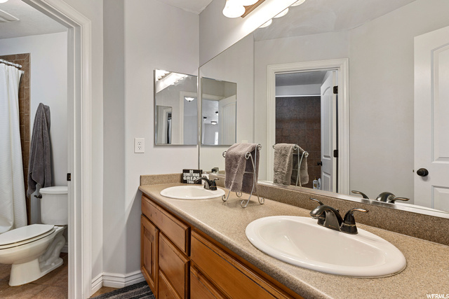 Bathroom featuring toilet, mirror, shower curtain, and double sink vanity