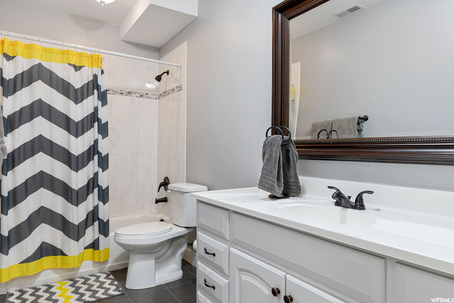 Full bathroom featuring tile floors, mirror, vanity, shower / bathing tub combination, toilet, and shower curtain