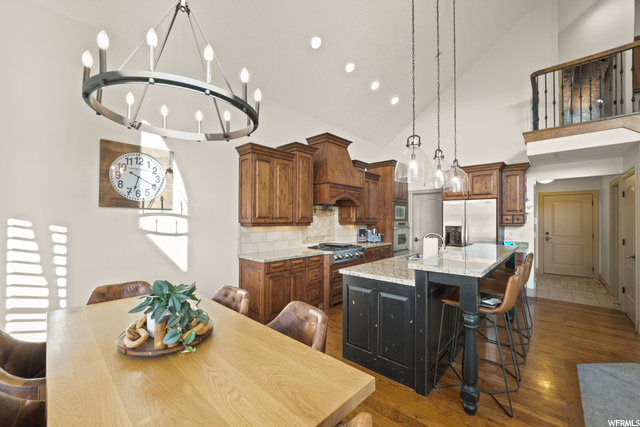 Kitchen featuring a center island, a breakfast bar area, natural light, gas stovetop, stainless steel refrigerator, exhaust hood, oven, light countertops, wood floors, and pendant lighting