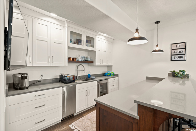 Kitchen featuring stainless steel beverage fridge, light countertops, pendant lighting, and white cabinetry