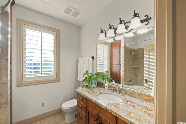 Shared bath with natural light, tile floors, toilet, mirror, and large vanity