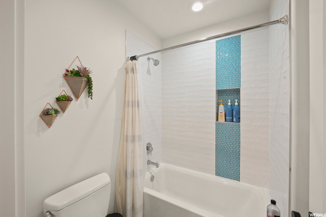 Bathroom with bathtub / shower combination, shower curtain, and toilet
