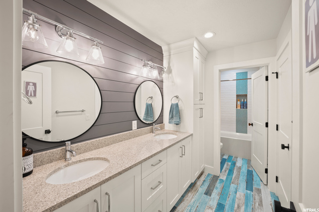 Bathroom Jack and Jill featuring mirror, dual bowl vanity, and shower / washtub combination