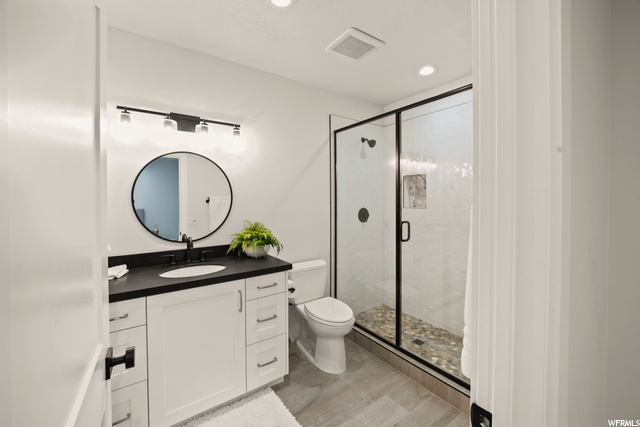 Full bathroom featuring toilet, oversized vanity, mirror, and shower with glass door