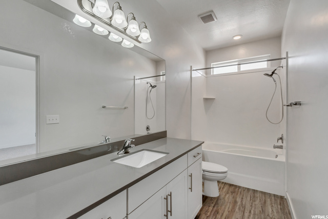 Full owners bathroom with laminate floor, vanity, toilet, mirror, and shower / bath combination