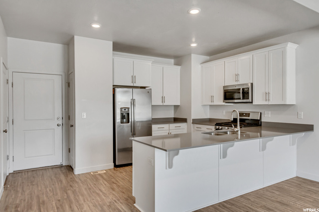 Kitchen featuring range oven, microwave, refrigerator, white cabinetry, and laminate flooring