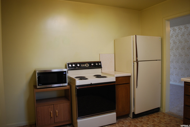 Kitchen featuring electric range oven, refrigerator, microwave, dark flooring, and light countertops