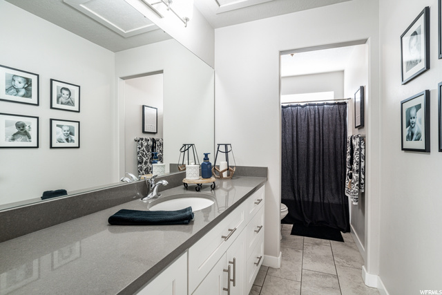 Bathroom with tile flooring, mirror, toilet, oversized vanity, and shower curtain