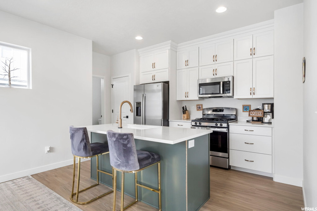 Kitchen featuring light hardwood floors, appliances with stainless steel finishes, light countertops, white cabinetry, and a kitchen island