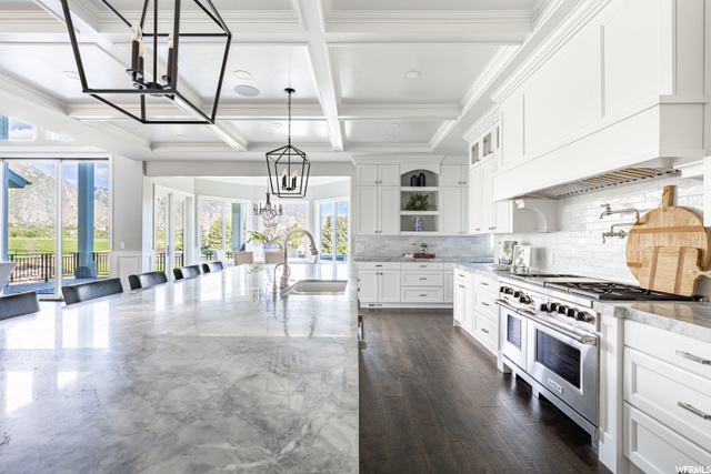 Kitchen featuring a wealth of natural light, hanging light fixtures, range with two ovens, backsplash, light countertops, coffered ceiling, wood-type flooring, and white cabinetry