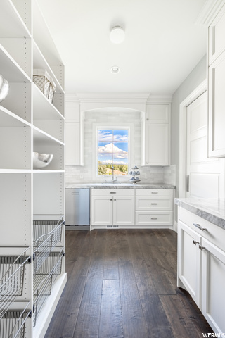 Kitchen with dark hardwood floors, light countertops, backsplash, and white cabinets