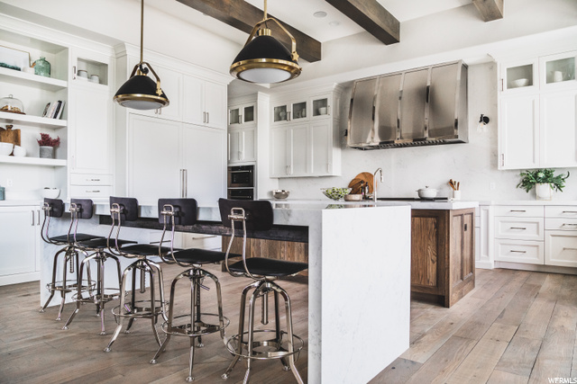 Kitchen with beamed ceiling, a center island, white cabinets, hanging light fixtures, and light hardwood floors