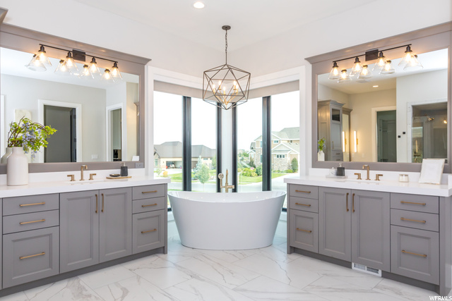 Bathroom with a bathtub, double sink vanity, mirror, and light tile flooring