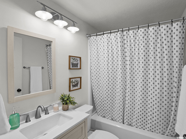 Full bathroom featuring vanity, shower / bath combination with curtain, mirror, and a textured ceiling