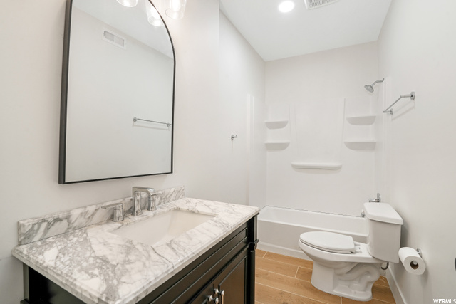 Full bathroom with oversized vanity, bathing tub / shower combination, light hardwood floors, and mirror