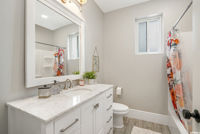 Full bathroom with vanity with extensive cabinet space, mirror, shower / tub combo, and light hardwood floors