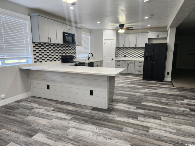 Kitchen featuring white cabinetry, black appliances, light countertops, light hardwood flooring, backsplash, and ceiling fan