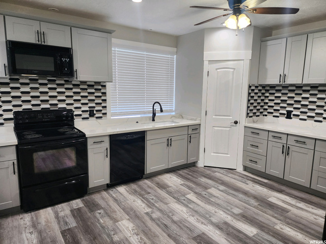 Kitchen featuring backsplash, white cabinets, light countertops, black appliances, light hardwood flooring, and ceiling fan