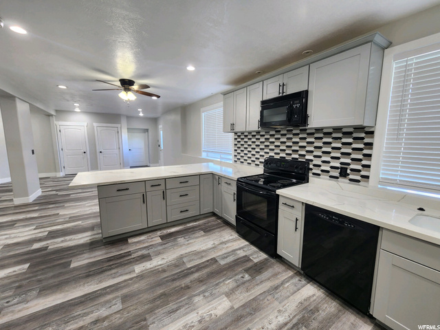 Kitchen with backsplash, light countertops, black appliances, white cabinetry, light hardwood flooring, and ceiling fan
