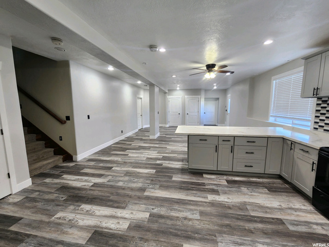 Kitchen with white cabinets, dark hardwood flooring, black range with electric stovetop, light countertops, and ceiling fan