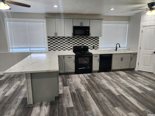 Kitchen with black appliances, white cabinets, hardwood floors, light countertops, backsplash, and ceiling fan