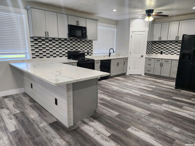 Kitchen featuring backsplash, white cabinets, light countertops, black appliances, light hardwood flooring, and ceiling fan